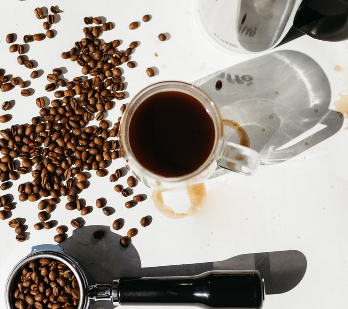 Black coffee in a glass mug with French press, coffee beans, espresso portafilter